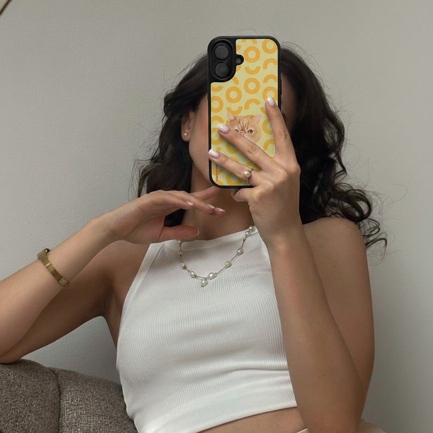 Person holding a phone with a yellow case featuring a pattern, wearing a white top and pearl necklace.