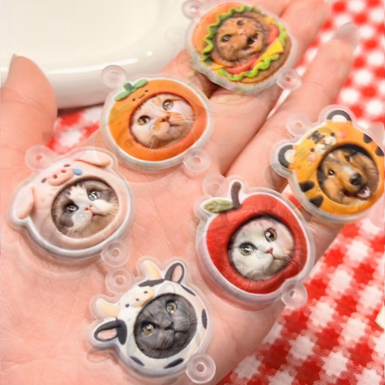 Five small animal figurines in clear plastic cases held in a hand with a red and white checkered background.