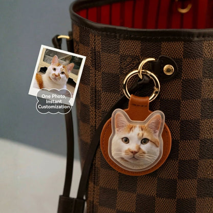 Cat-shaped keychain attached to a checkered handbag with a photo of a cat on a small card.